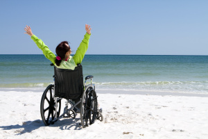 image of woman in wheelchair on beach with arms raised in victory