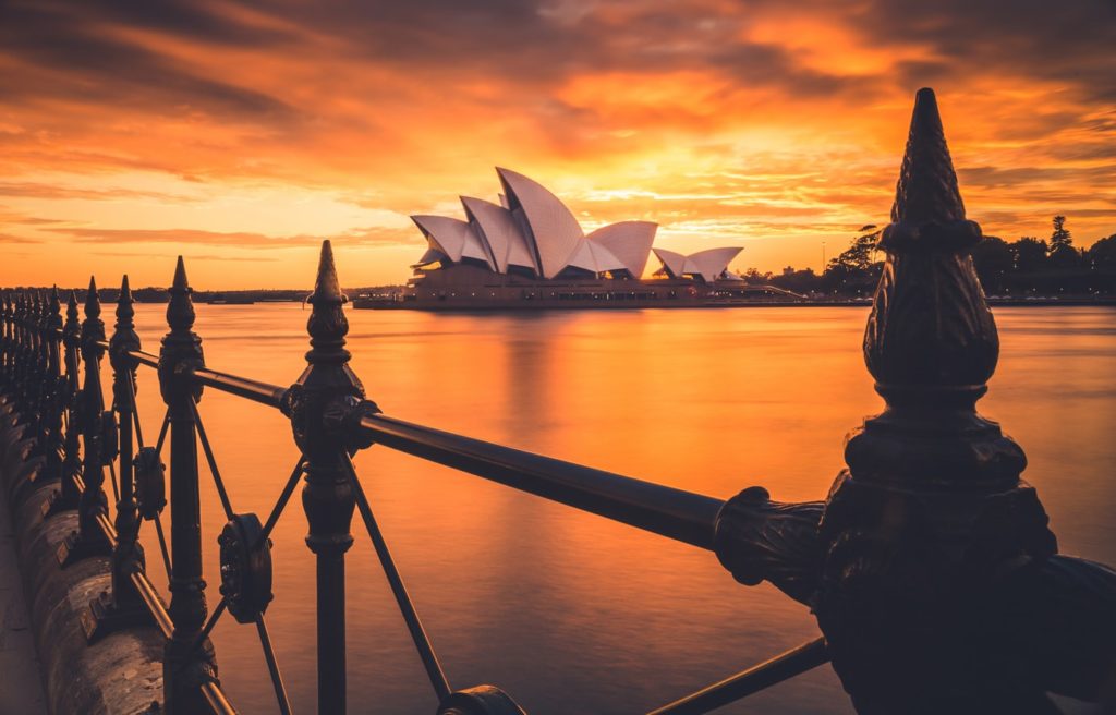 Australia photo by Liam Pozz | Abroad101 Blog Sydney Opera House at sunset across Sydney Harbour, with iron railings in the foreground.