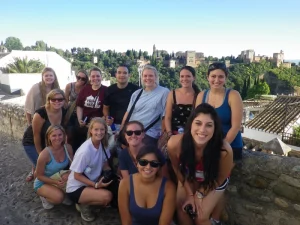 Students attending Arcos Learning Abroad program in Granada, Spain | Abroad101 Blog Group of students studying abroad with the Arcos Learning Abroad program, smiling together with the Alhambra palace visible in the background in Granada, Spain.
