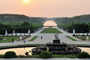 b | Abroad101 Blog View of the Gardens of Versailles at sunset, featuring a large fountain with statues in the foreground and the Grand Canal stretching into the distance.