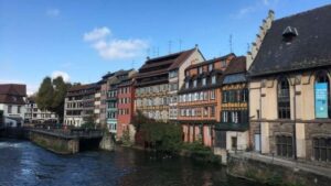 e | Abroad101 Blog View of traditional half-timbered houses along the river in Strasbourg, France, under a clear blue sky.