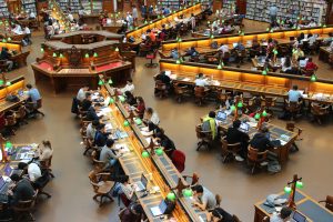pexels-pixabay-159775 | Abroad101 Blog Overhead view of students studying at long wooden tables under green lamps in a grand library reading room.