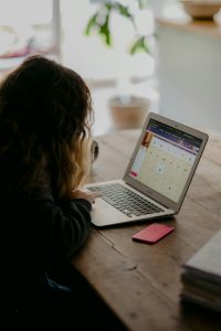 Student uses digital tools on a laptop at a wooden desk, highlighting technology‑powered learning and remote classroom engagement.