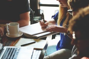 pexels-startup-stock-photos-7096 | Abroad101 Blog Young professionals collaborate at a café-style table, writing in notebooks and sharing ideas—illustrating the benefits of peer-supported learning.