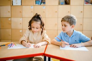 pexels-anastasia-shuraeva-8466765 | Abroad101 Blog Two children draw with colored pencils at a classroom table, focused on their artwork in a bright room with wooden cubbies.