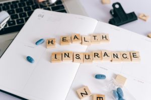 pexels-leeloothefirst-7163956 | Abroad101 Blog Scrabble tiles spelling ‘HEALTH INSURANCE’ on a planner beside blue pills, illustrating health coverage planning for international students studying abroad.