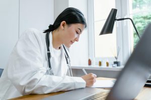 pexels-tima-miroshnichenko-8376233 | Abroad101 Blog Doctor in a white coat writing notes at a desk in a clinic office, symbolizing visiting a healthcare provider and managing medical care while studying abroad.
