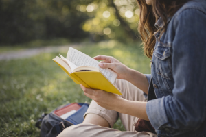 Student reading while Abroad | Abroad101 Blog Student reading a book outdoors on the grass with a backpack nearby in a peaceful study setting