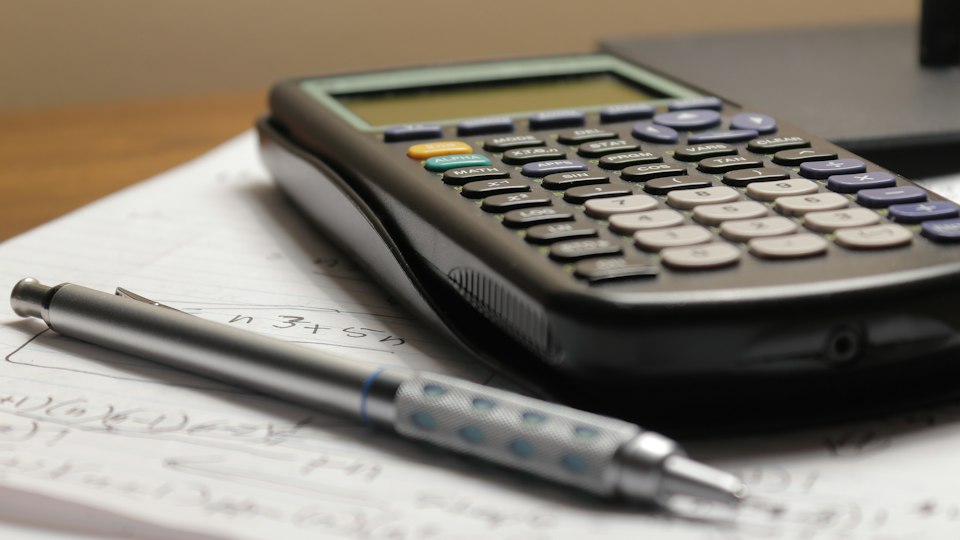 Calculator, pen and financial worksheet on a desk representing study abroad budgeting.